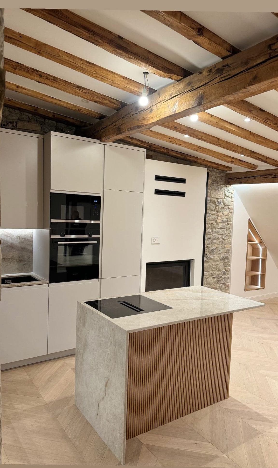 Cuisine rénovée sous poutres apparentes, avec spots encastrés au plafond et niche éclairée par LED