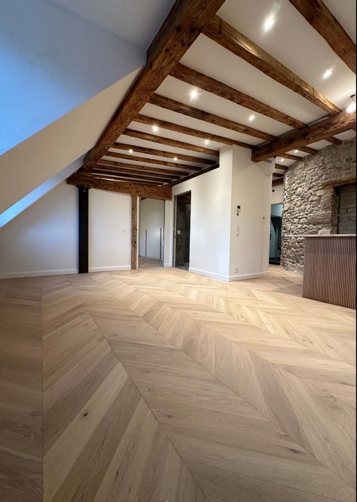Combles aménagés avec parquet en point de Hongrie et spots LED encastrés entre les poutres