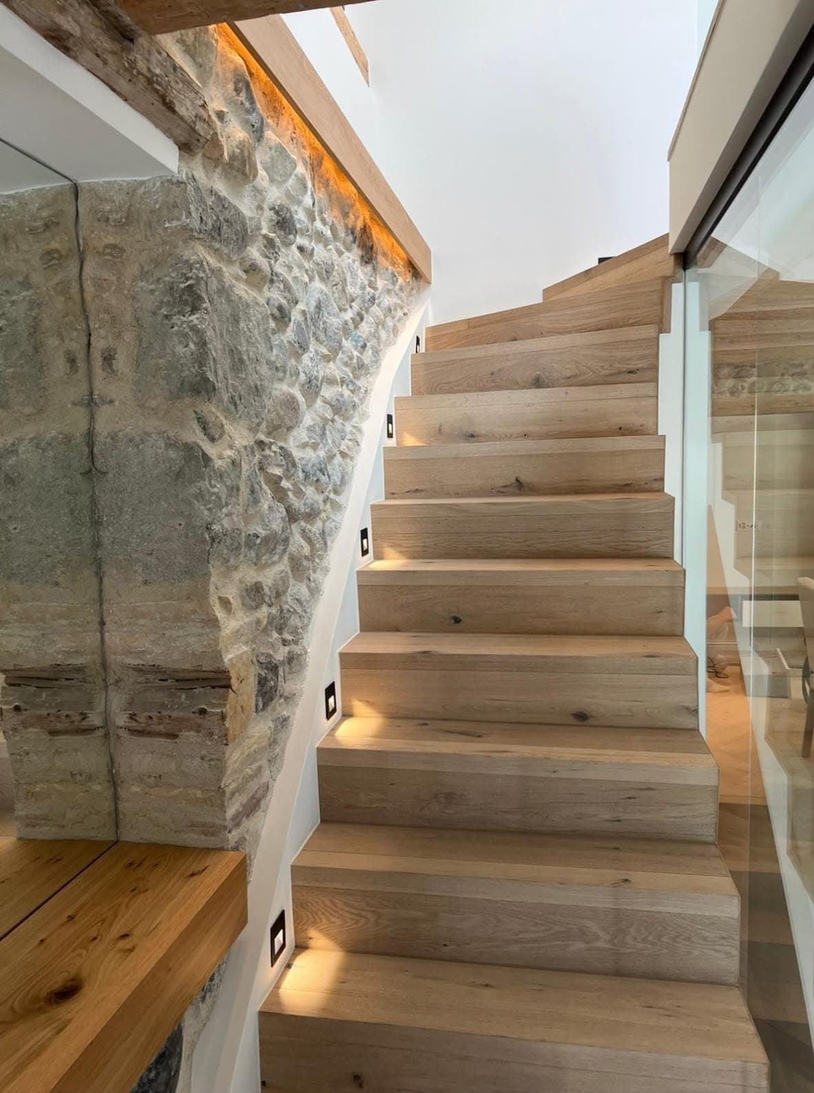 Escalier en bois le long d'un mur en pierre, avec balisage LED des marches et ruban lumineux sous la main courante