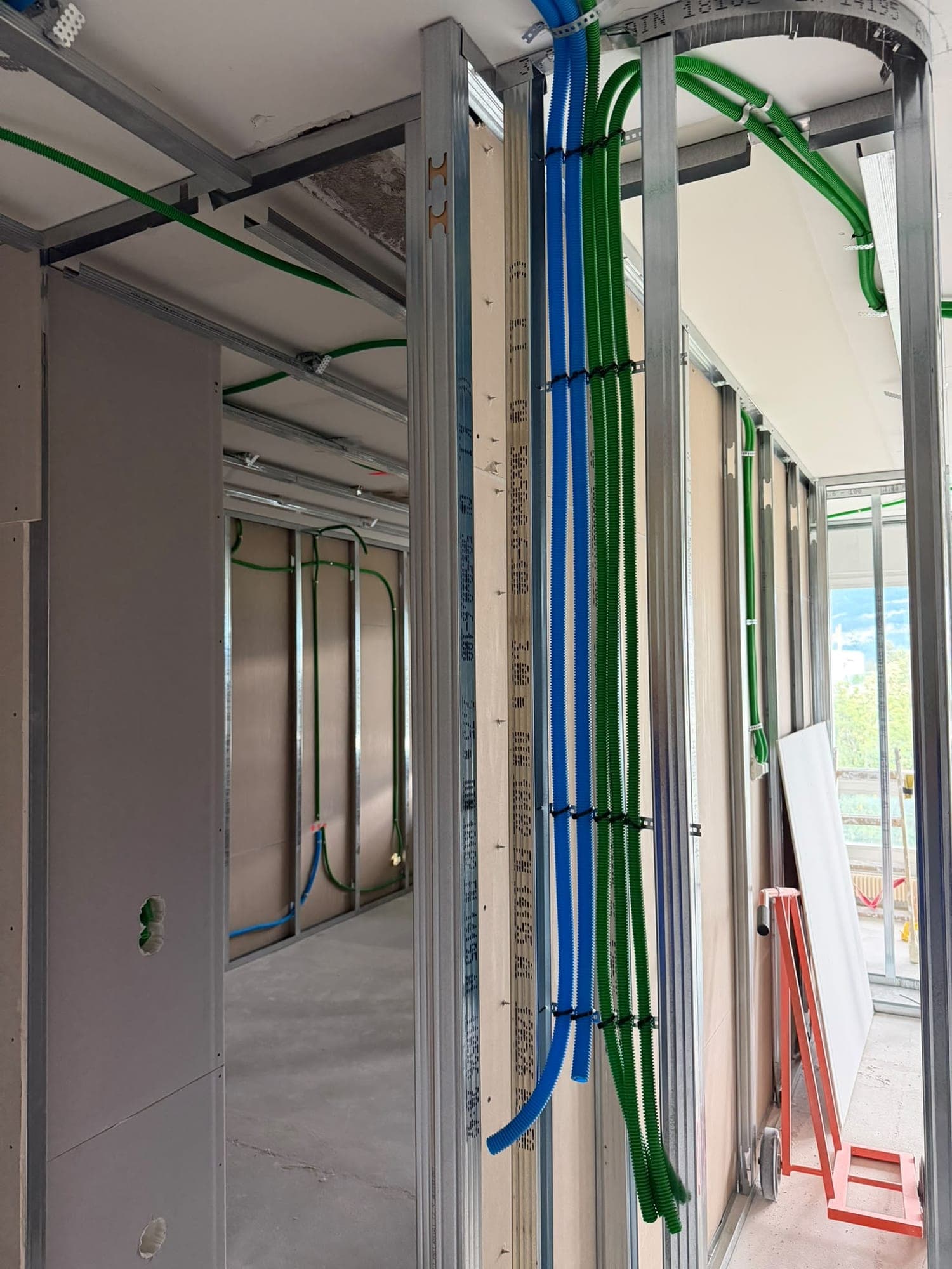 Cloison en construction avec faisceau de gaines électriques bleues et vertes fixées sur l'ossature métallique