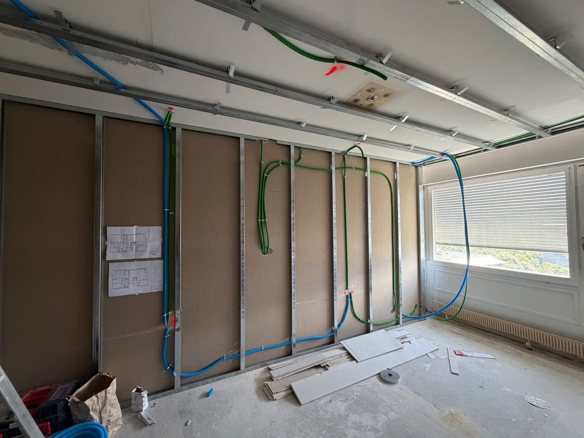 Cloison ouverte montrant le cheminement des gaines électriques et les plans d'installation affichés au mur